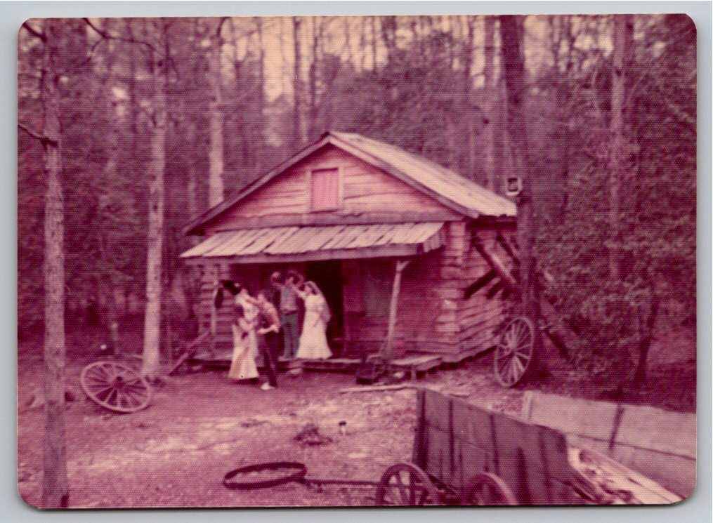 Vintage 1970s Color Snapshot: Rustic Log Cabin with Wagon Wheels
